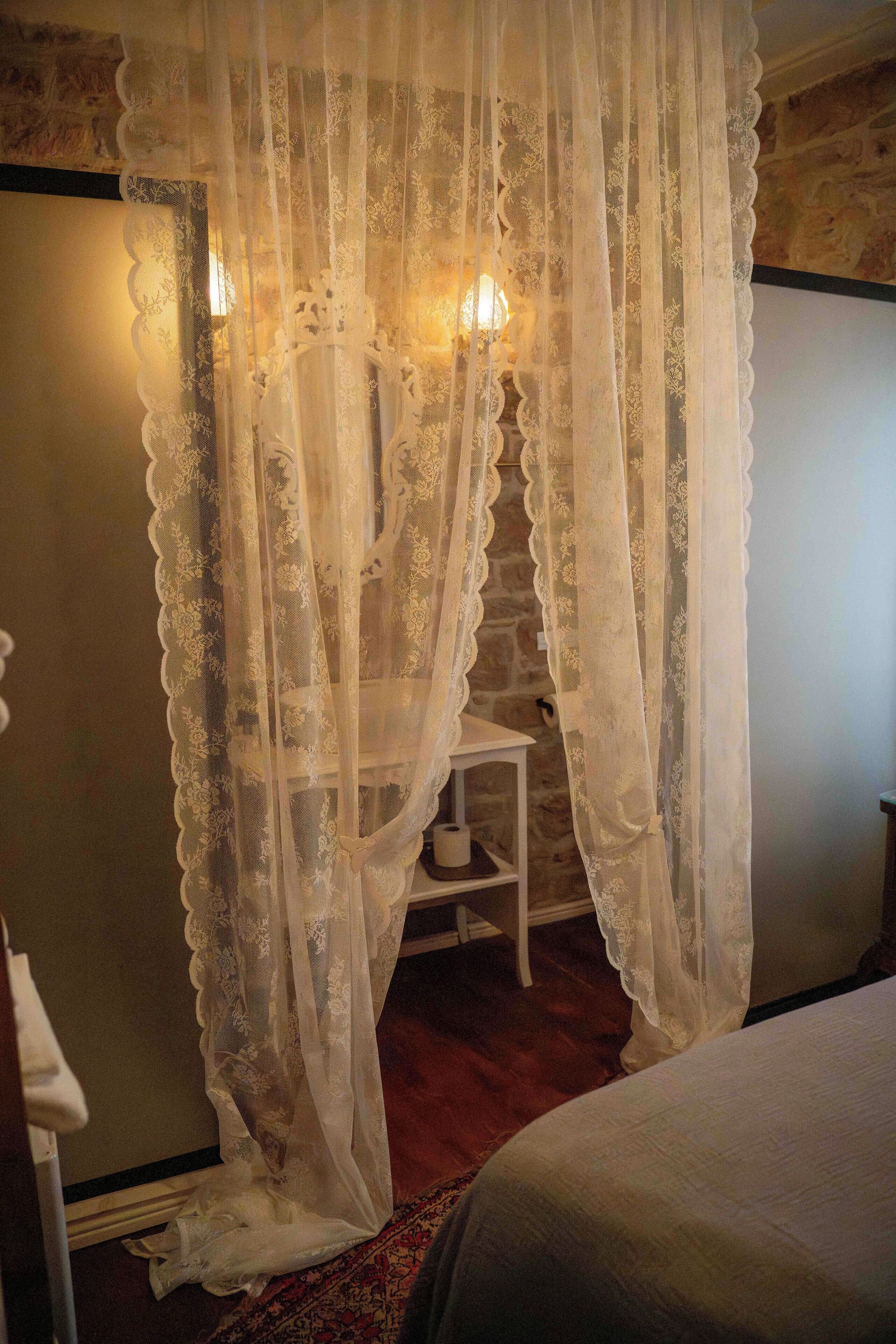 A room with a bed, a small table, and a chair. There is a decorative curtain with a floral pattern.