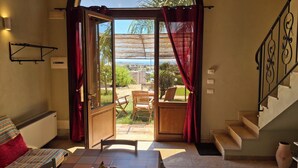 A room with a dining table, chairs, a fruit bowl, a sofa, a staircase, and a view of the outdoors. - La Vela in Sampieri 2 minutes from the sea, villa with pool. (Sicilia)
