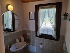 A bathroom with a round mirror, a sink, a window with a curtain, and a framed certificate on the wall.