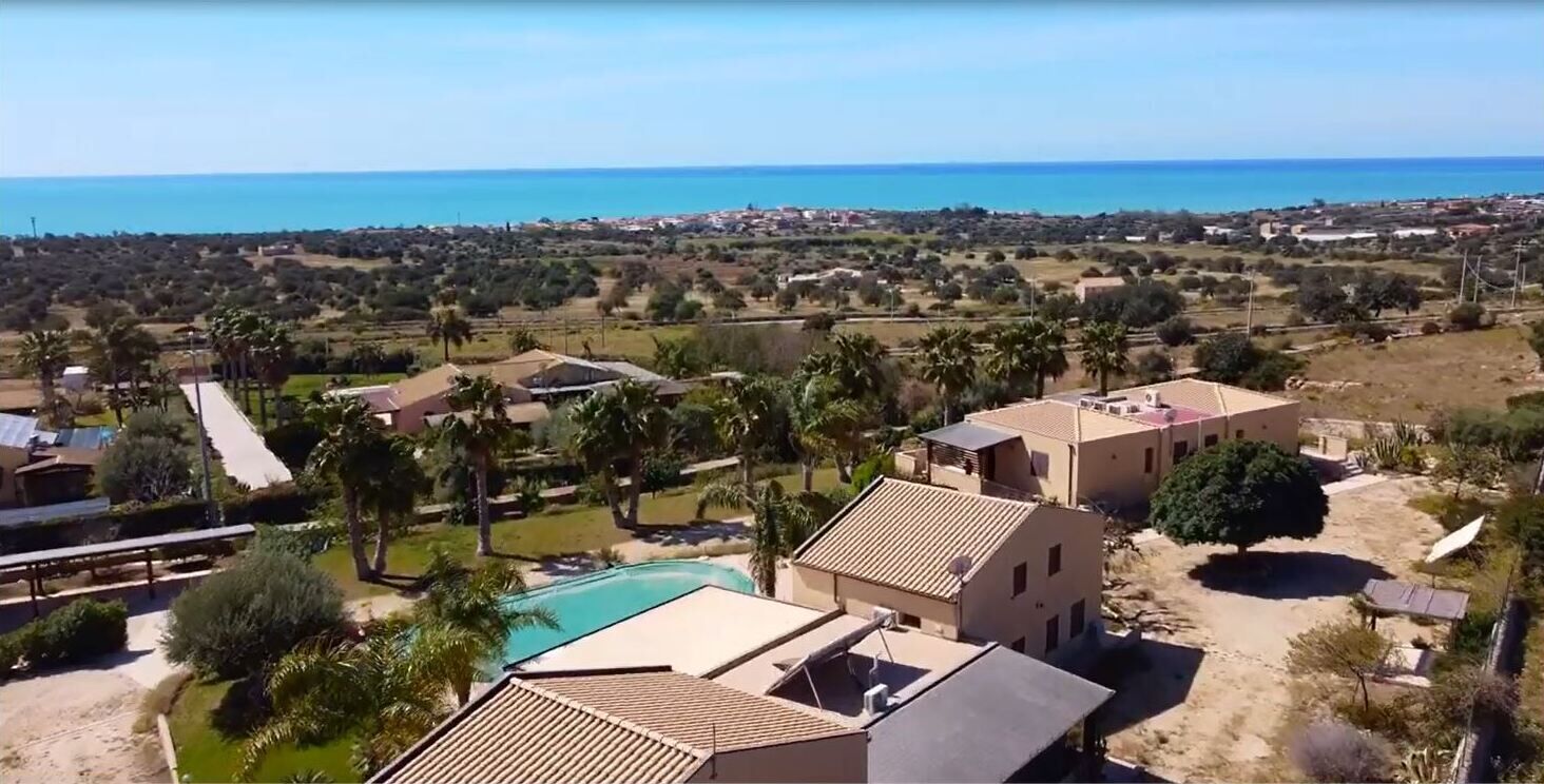 A residential area with a swimming pool, houses, and a view of the sea.