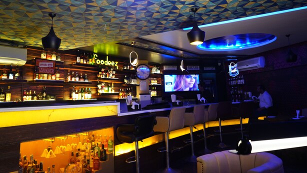 Un bar con un diseño geométrico en el techo, un reloj y un letrero de neón.