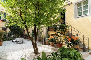 A courtyard with a dining table and chairs, surrounded by potted plants and a staircase. - Dimora Paolina, a charming villa with a secret garden, in the historic center of Lucca (Lucca)
