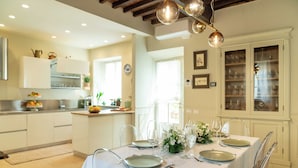 A modern kitchen with white cabinets, a dining area set for six with clear chairs, and a chandelier. - Dimora Paolina charming villa with secret garden, in the historical center of Lucca (Lucca)