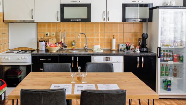 Una cocina moderna con gabinetes blancos, microondas, estufa, lavavajillas y refrigerador. Hay una mesa de comedor con sillas y un menú encima.
