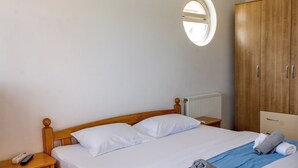 Una cama bien tendida con sábanas blancas, un cabecero de madera, una mesita de noche con un control remoto y un armario con espejo.