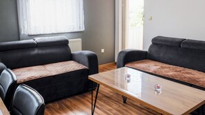 Una sala de estar moderna con dos sofás negros, una mesa de centro de madera y un ventanal con cortinas blancas.