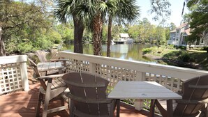 A wooden deck with outdoor furniture, a view of a lake, and a house in the background. - Lagoonside Luxury • 5 min Walk to Beach • Pool, Hot Tub & Kiddie Pool (Hilton Head Island)