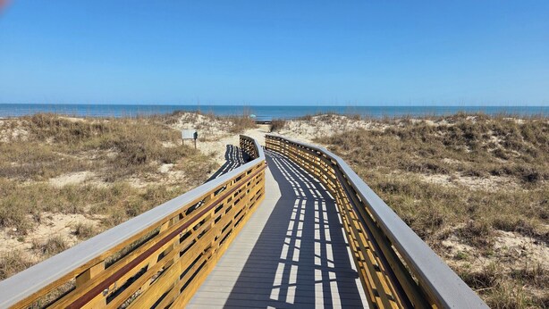 A wooden boardwalk leading to the beach, surrounded by sand dunes and sparse vegetation. - Lagoonside Luxury • 5 min Walk to Beach • Pool, Hot Tub & Kiddie Pool (Hilton Head Island)