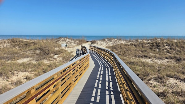 A wooden boardwalk leading to the beach, surrounded by sand dunes and sparse vegetation. - Lagoonside Luxury • 5 min Walk to Beach • Pool, Hot Tub & Kiddie Pool (Hilton Head Island)