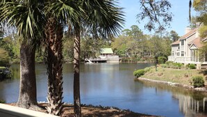 A lake with a dock and a building with a green roof. - Lagoonside Luxury • 5 min Walk to Beach • Pool, Hot Tub & Kiddie Pool (Hilton Head Island)