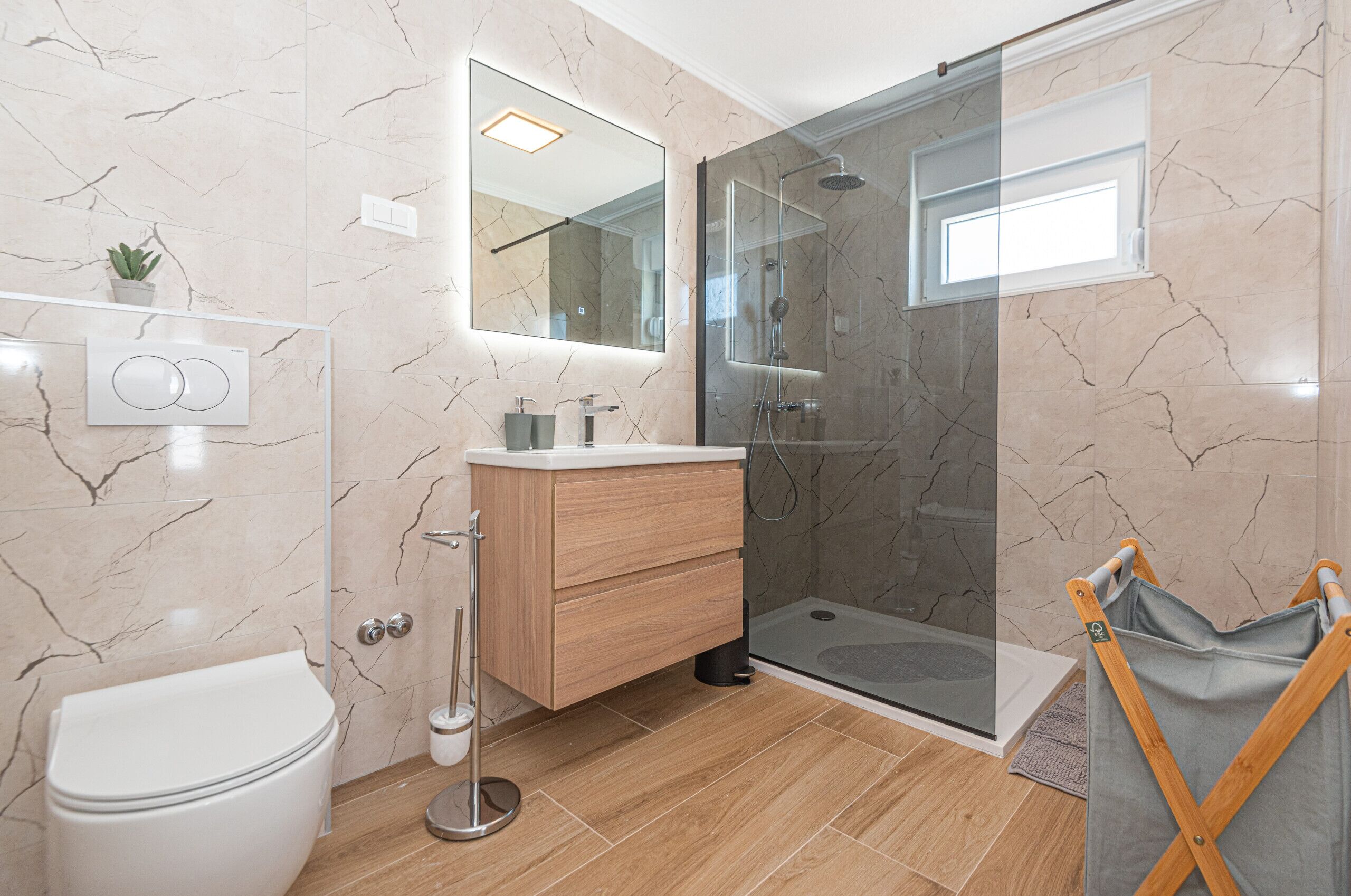 Un baño moderno con inodoro, tocador, ducha y zona de ducha con mampara de vidrio.