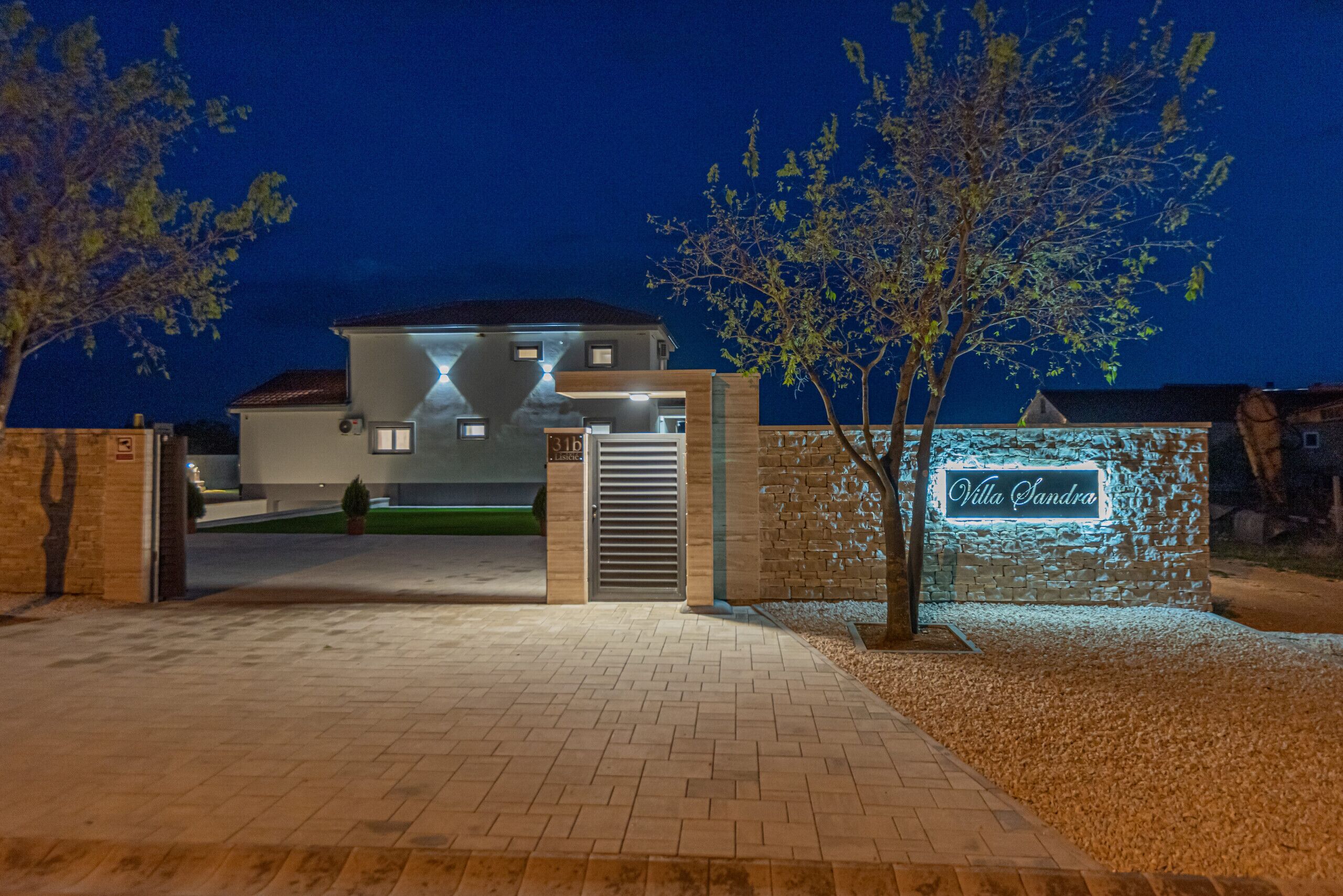 A modern villa with a gated entrance, a well-maintained driveway, and a neon sign.