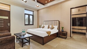 A modern hotel room with a large bed, a small table, a chair, and a wardrobe. - Miranda by Akama Homes (Noida)