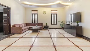 A spacious living room with a sectional sofa, a coffee table, a flat-screen TV, and a large tiled floor. - Miranda by Akama Homes (Noida)