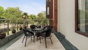 A balcony with a round table and four chairs, potted plants, and a view of trees and buildings. - Miranda by Akama Homes (Noida)