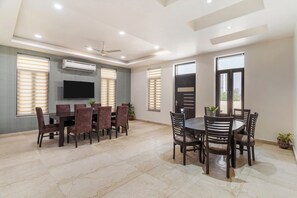 A spacious dining area with a large table and chairs, an air conditioning unit, and a flat-screen TV mounted on the wall.