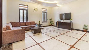 A modern living room with a sectional sofa, a coffee table, a flat-screen TV, and potted plants. - Miranda by Akama Homes (Noida)