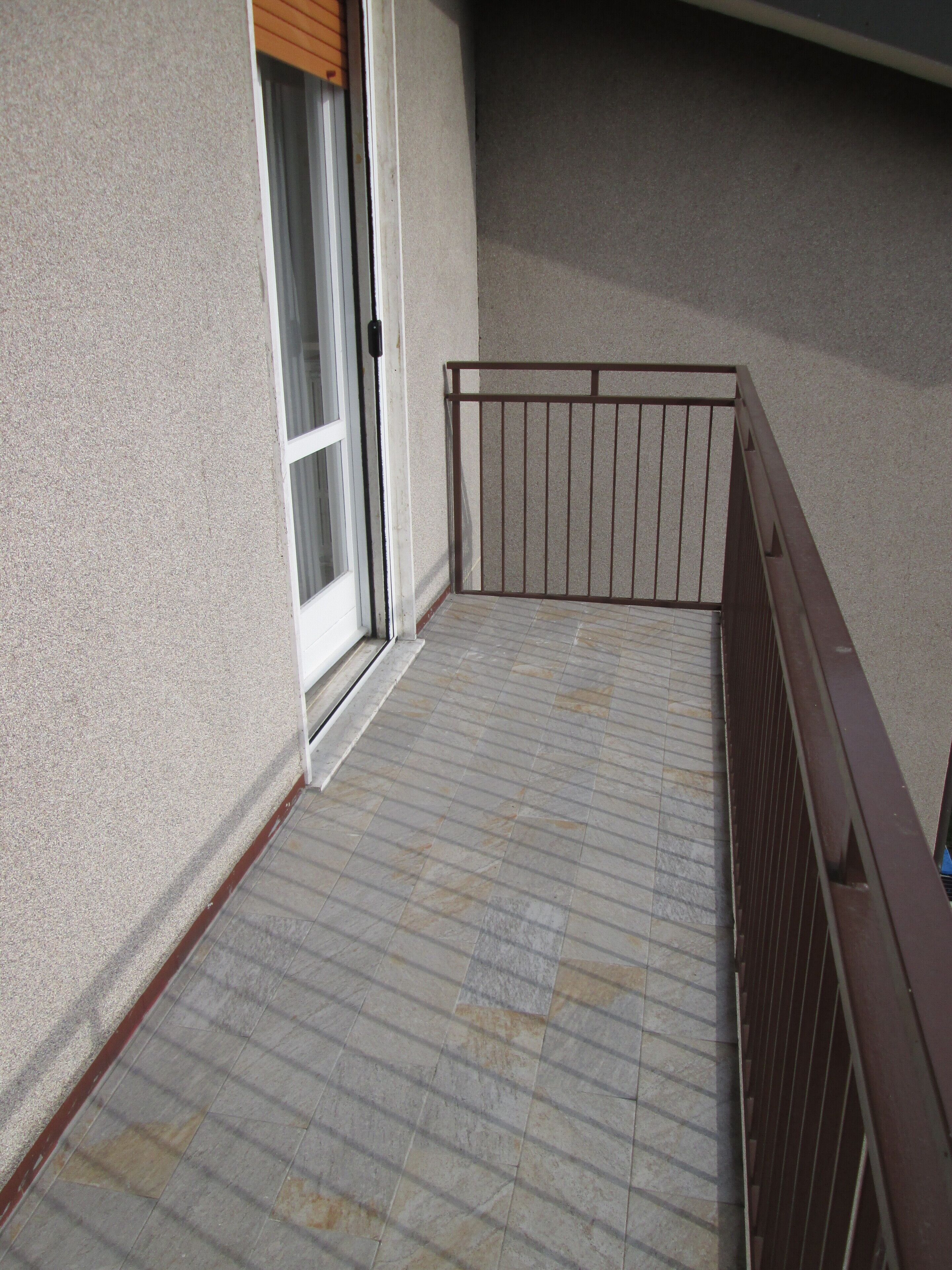 Ein Balkon mit Metallgeländer, eine Tür mit Fenster und ein Fliesenboden.