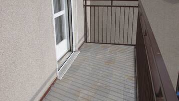 Ein Balkon mit Metallgeländer, eine Tür mit Fenster und ein Fliesenboden.