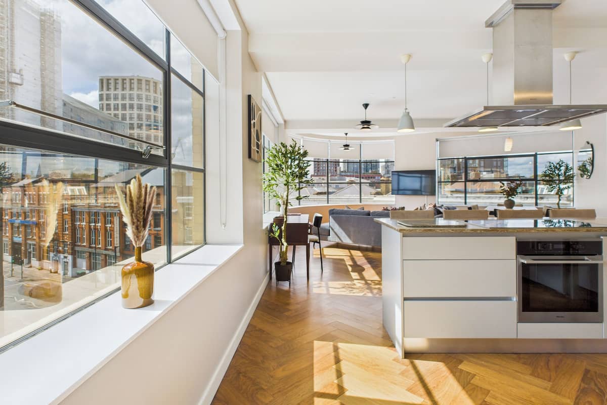 Una cocina moderna con una isla grande, una zona de comedor con sofá y vistas de la ciudad a través de amplios ventanales.