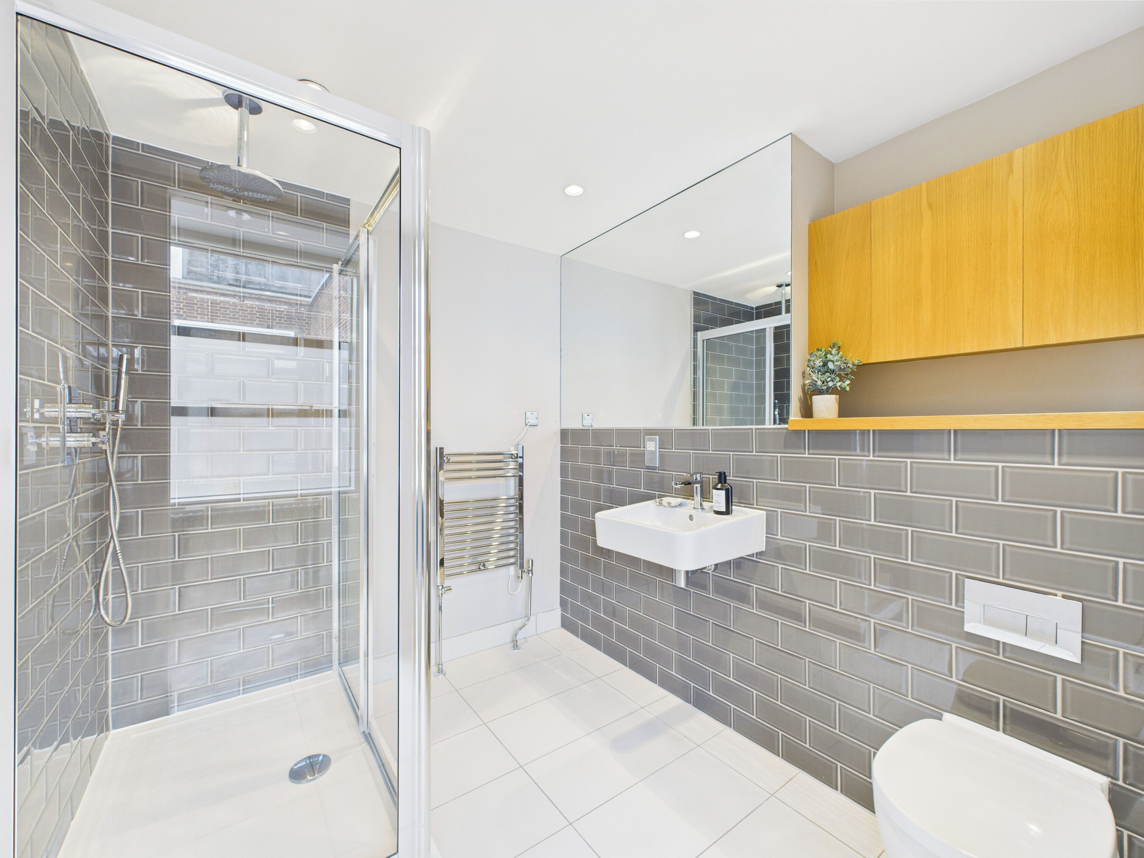 A modern bathroom with a glass-enclosed shower, a white sink, and a wooden cabinet above the mirror.