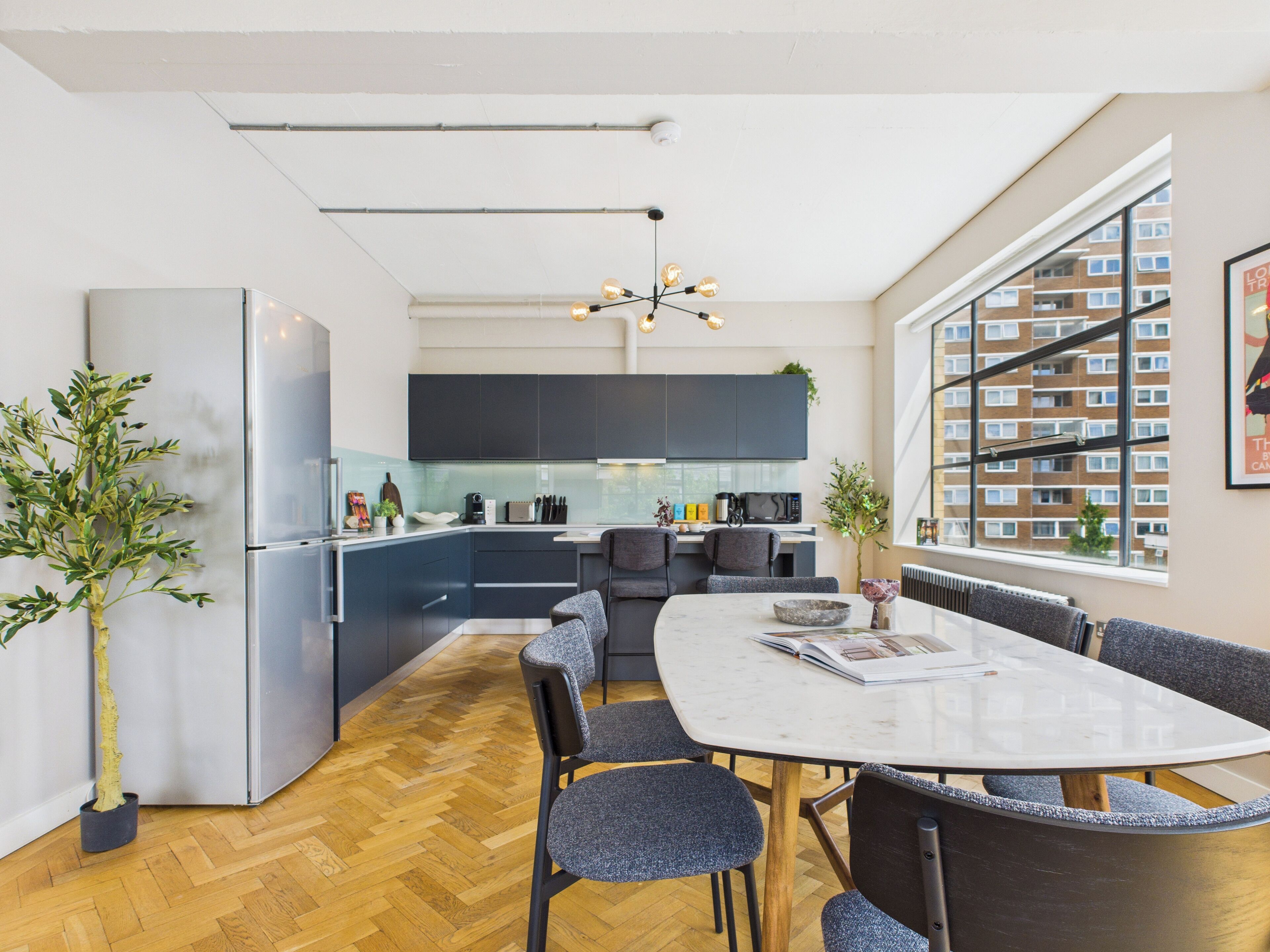 Eine moderne Küche mit dunklen Schränken, einem Edelstahlkühlschrank und einem großen Fenster.