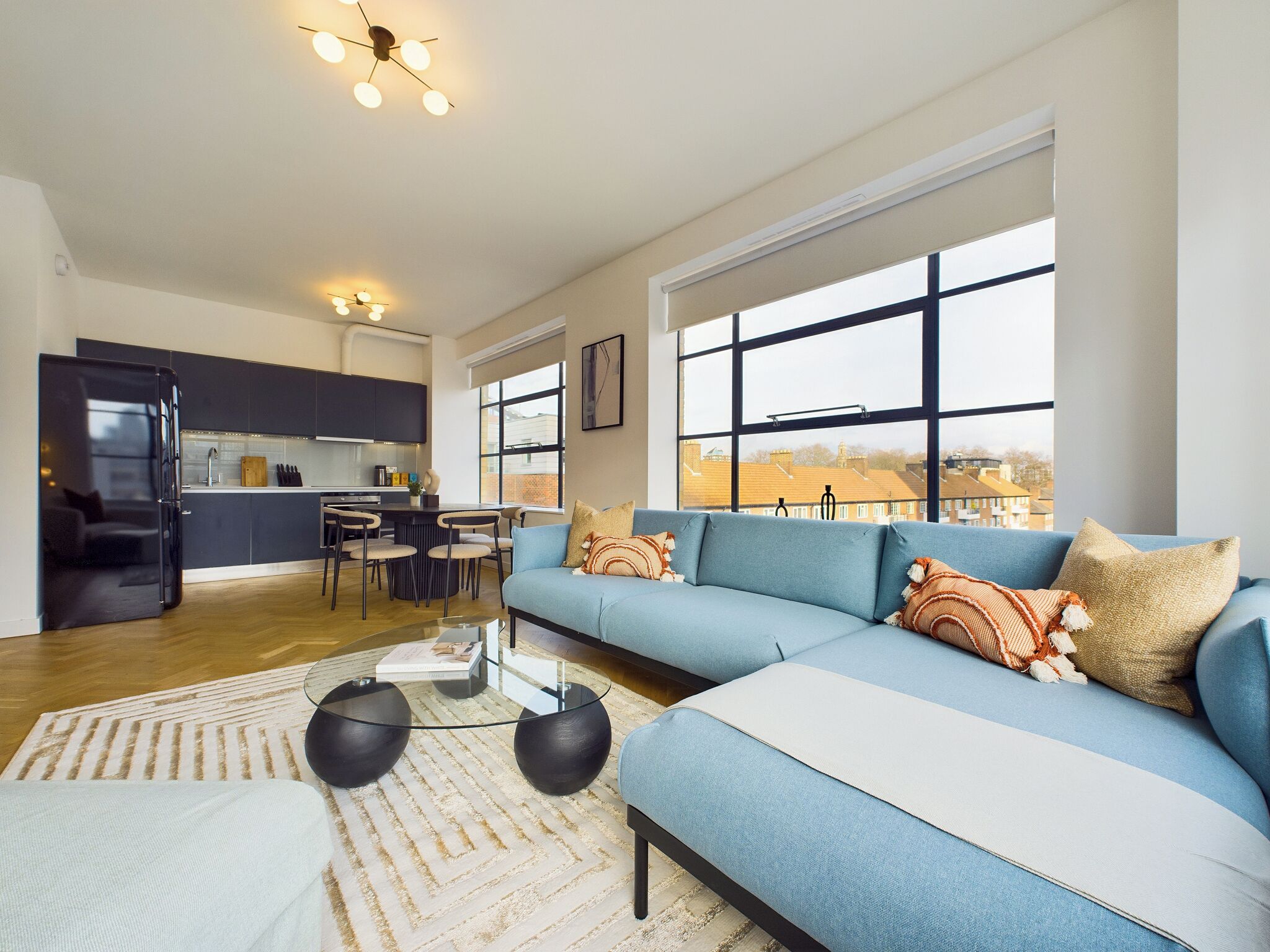 A modern living room with a blue sofa, a glass coffee table, and a kitchen in the background.