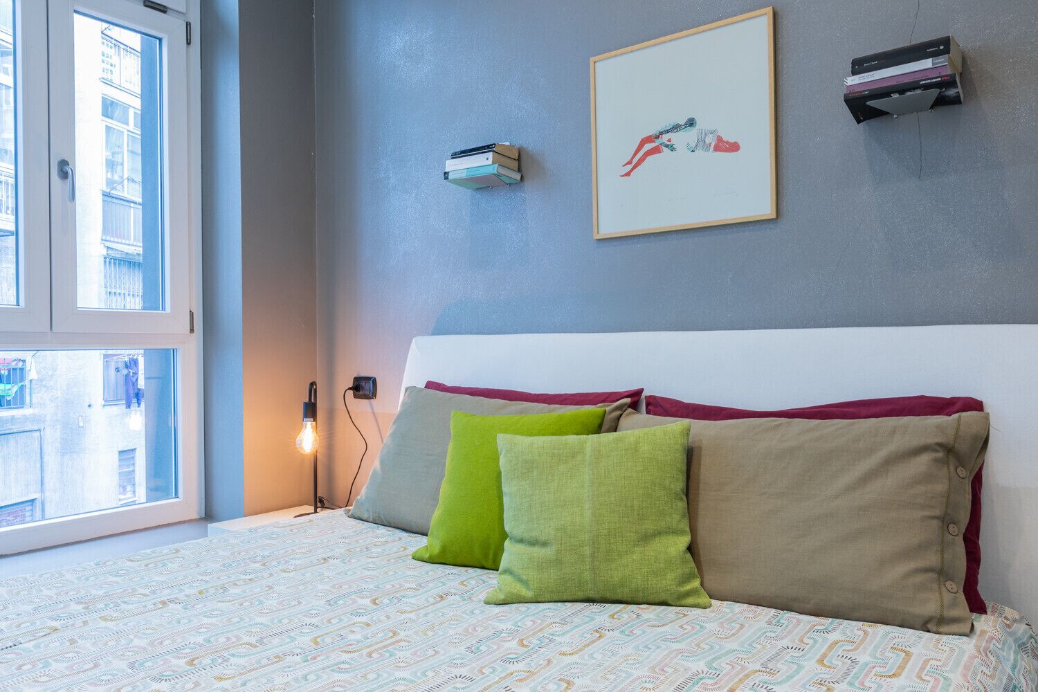 Ein Schlafzimmer mit Bett, Kissen, einer Nachttischlampe und einem gerahmten Bild an der Wand.