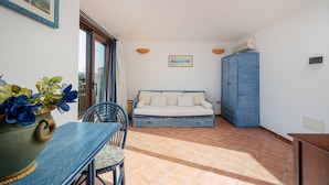 A room with a sofa, a dining table with chairs, a cabinet, and a painting on the wall. - Loft delle brezze by Wonderful Italy (Olbia)