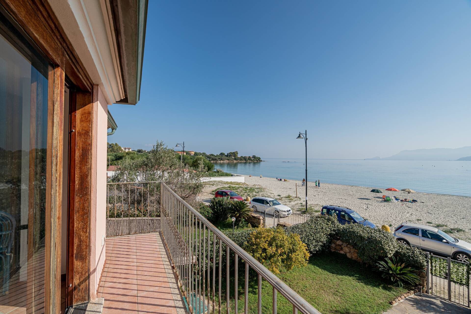 A balcony with a view of a beach, cars parked on the beach, and a clear sky.
