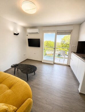 A modern living room with a sofa, a coffee table, a flat-screen TV, and a sliding glass door leading to an outdoor area.