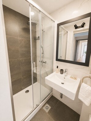 Un baño moderno con ducha de vidrio, lavamanos blanco y un espejo grande.