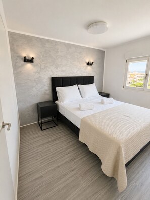 Un dormitorio moderno con una cama grande, dos mesitas de noche, una mesita auxiliar, un ventanal con vistas y una pared con textura.