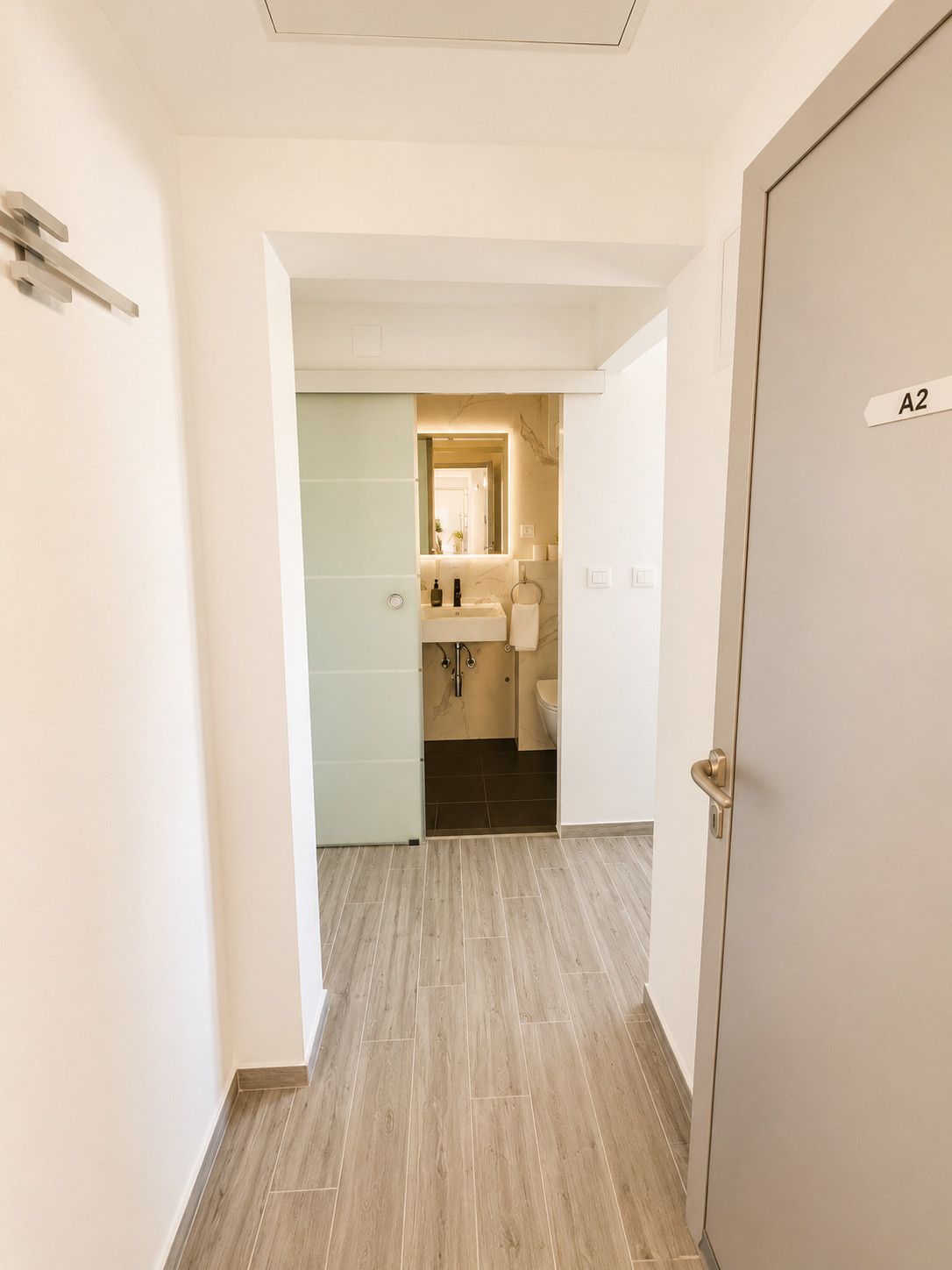 Ein Flur, der zu einem Badezimmer mit Toilette, Waschbecken und Spiegel führt.