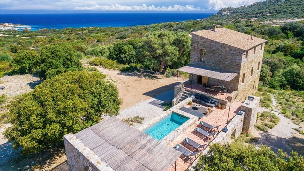 A stone villa with a swimming pool, outdoor seating, and a view of the sea.
