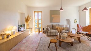 A cozy living room with a sofa, coffee table, and chairs, a wooden console table with a lamp, and a large window with natural light.
