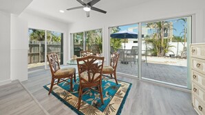A spacious dining area with a ceiling fan, large windows, and a view of the backyard. - Tipsy Turtle: Charming 3-Bedroom Beach Cottage! (Sanibel)