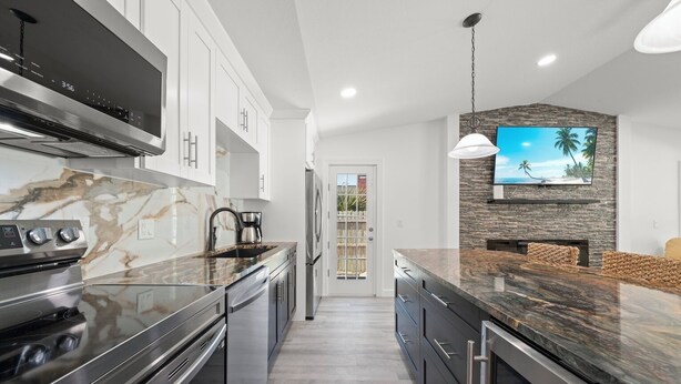 A modern kitchen with stainless steel appliances, marble countertops, and a stone backsplash. - Tipsy Turtle: Charming 3-Bedroom Beach Cottage! (Sanibel)