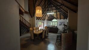 A spacious dining area with a wooden table and chairs, a staircase, and a thatched ceiling. - Singwe Private Safari lodge (Marloth Park)