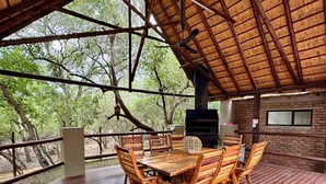 Un área de comedor al aire libre con una mesa y sillas de madera, un muro de ladrillo y un techo de paja.