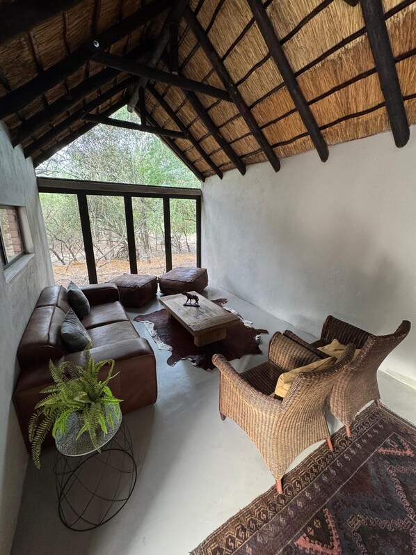 A cozy lounge area with a thatched roof, leather sofas, a woven chair, and a central wooden coffee table.
