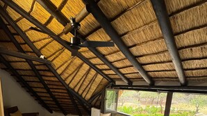 Un dormitorio con techo inclinado, una cama con ropa blanca, una silla de mimbre y vistas al verdor exterior.