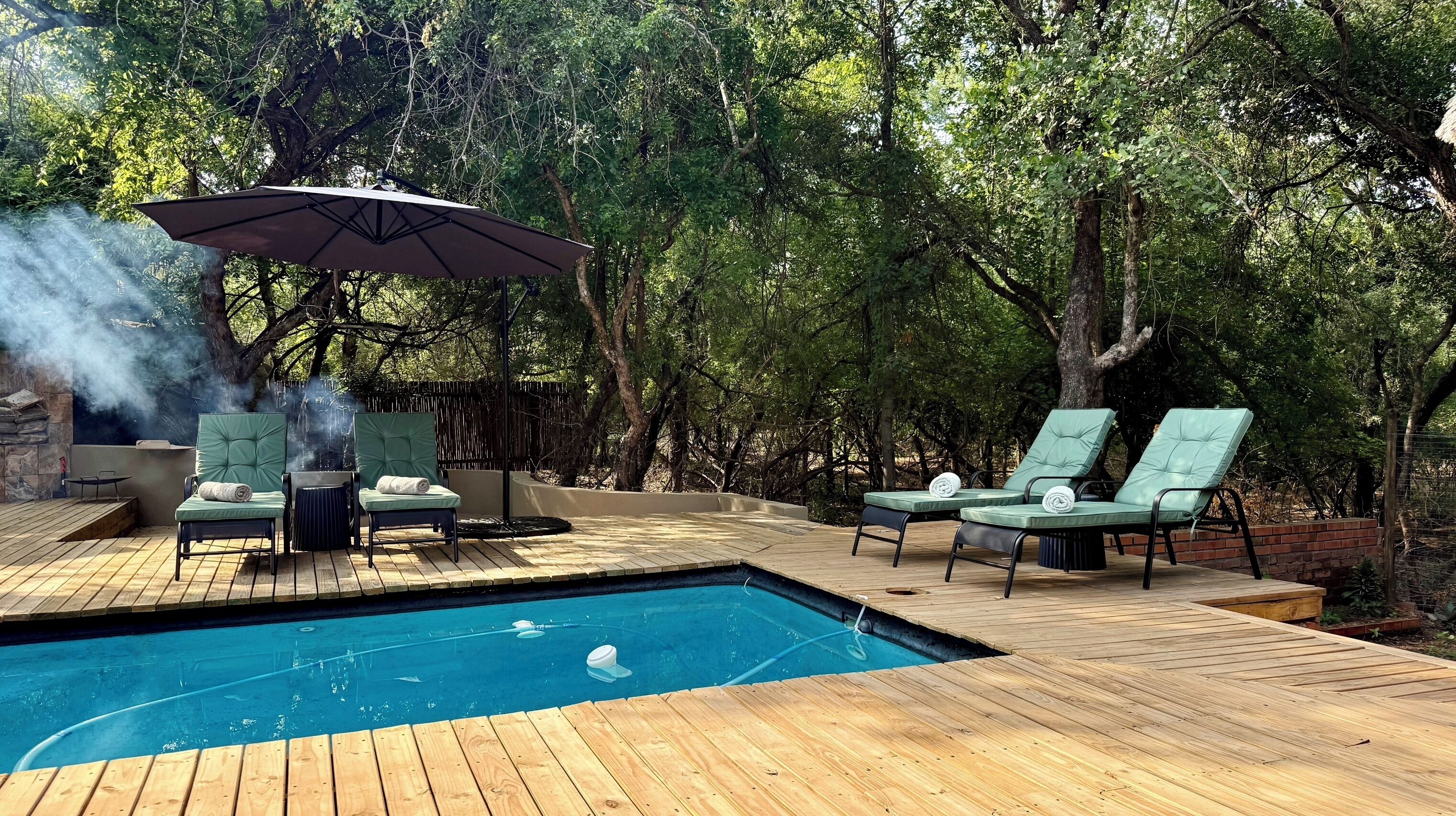 A poolside area with a wooden deck, lounge chairs, and a barbecue grill.