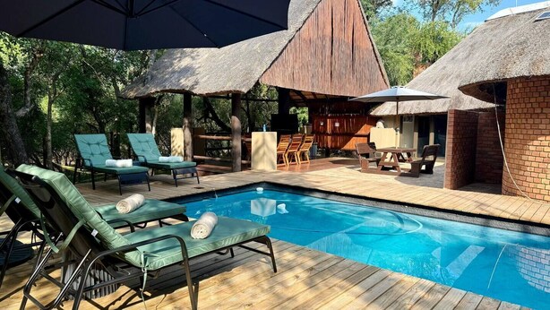 Un área junto a la piscina con sillas de descanso, una terraza de madera y estructuras con techo de paja.