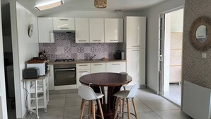 A compact kitchen with white cabinets, a round wooden table, and two white chairs.