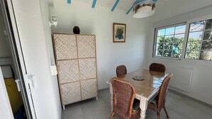 A dining area with a wooden table and wicker chairs, a decorative cabinet, and a window with a view of greenery.