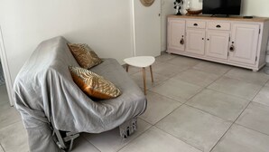 A living room with a grey sofa, a small white table, and a cabinet with a TV.