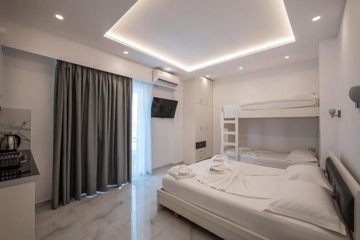 Una habitación de hotel moderna con una cama grande, una cama litera, un televisor de pantalla plana y una kitchenette.