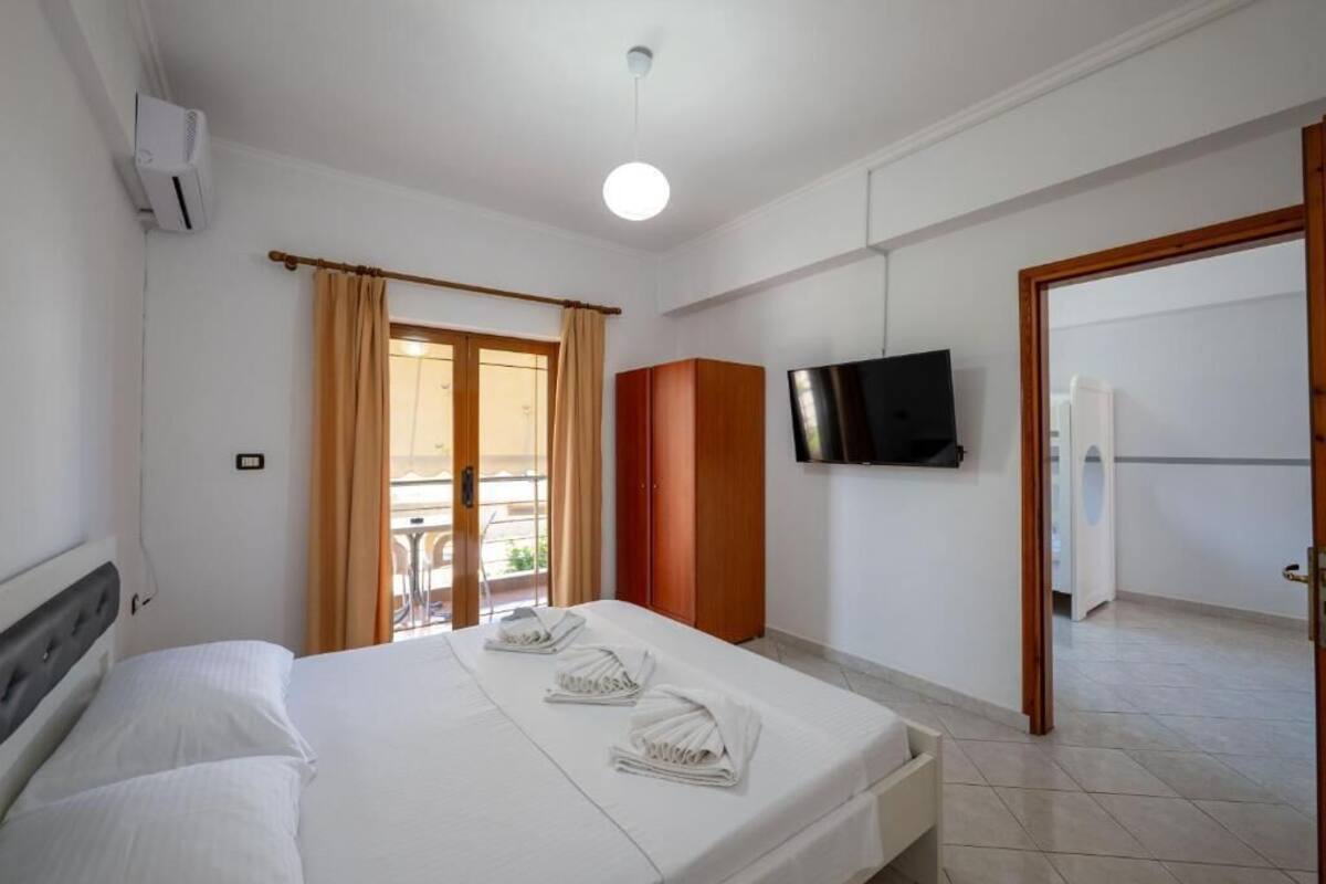 Una habitación de hotel con una cama, un televisor en la pared y un balcón con cortinas.
