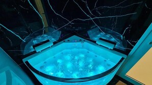 Een moderne badkamer met een glazen bubbelbad, een douchegedeelte en een vloer van marmer.